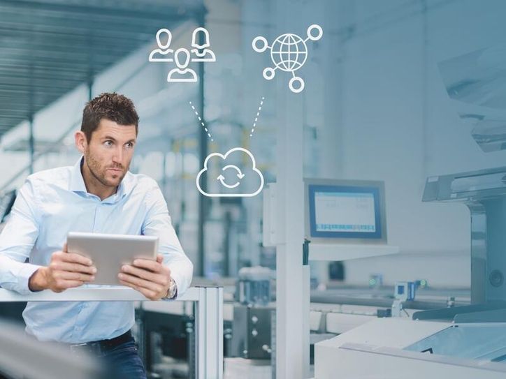 Mann mit Tablet in einer Fertigungshalle, darüber Symbole für Team, Cloud und weltweite Vernetzung